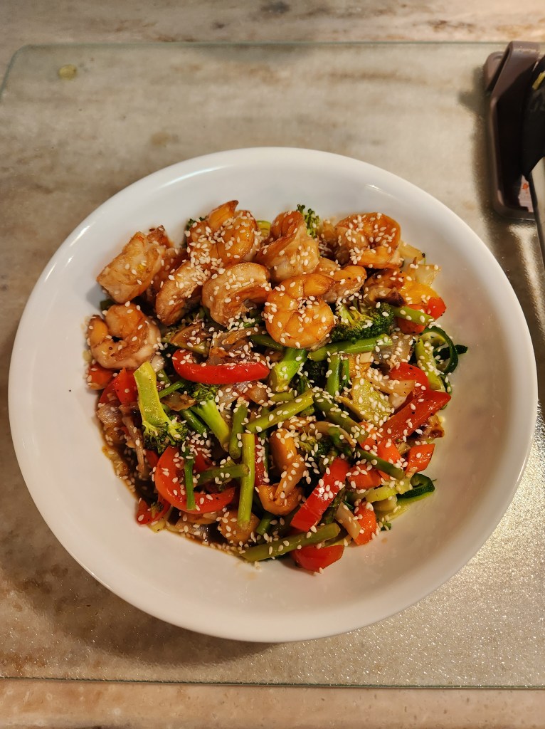 Stirfried shrimp with veggies topped with sesame seeds.