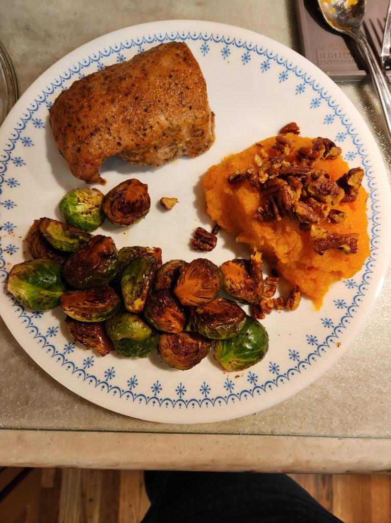 A chicken thigh cooked to perfection with mashed sweet potatoes topped with toasted pecans and crispy brussels sprouts.
