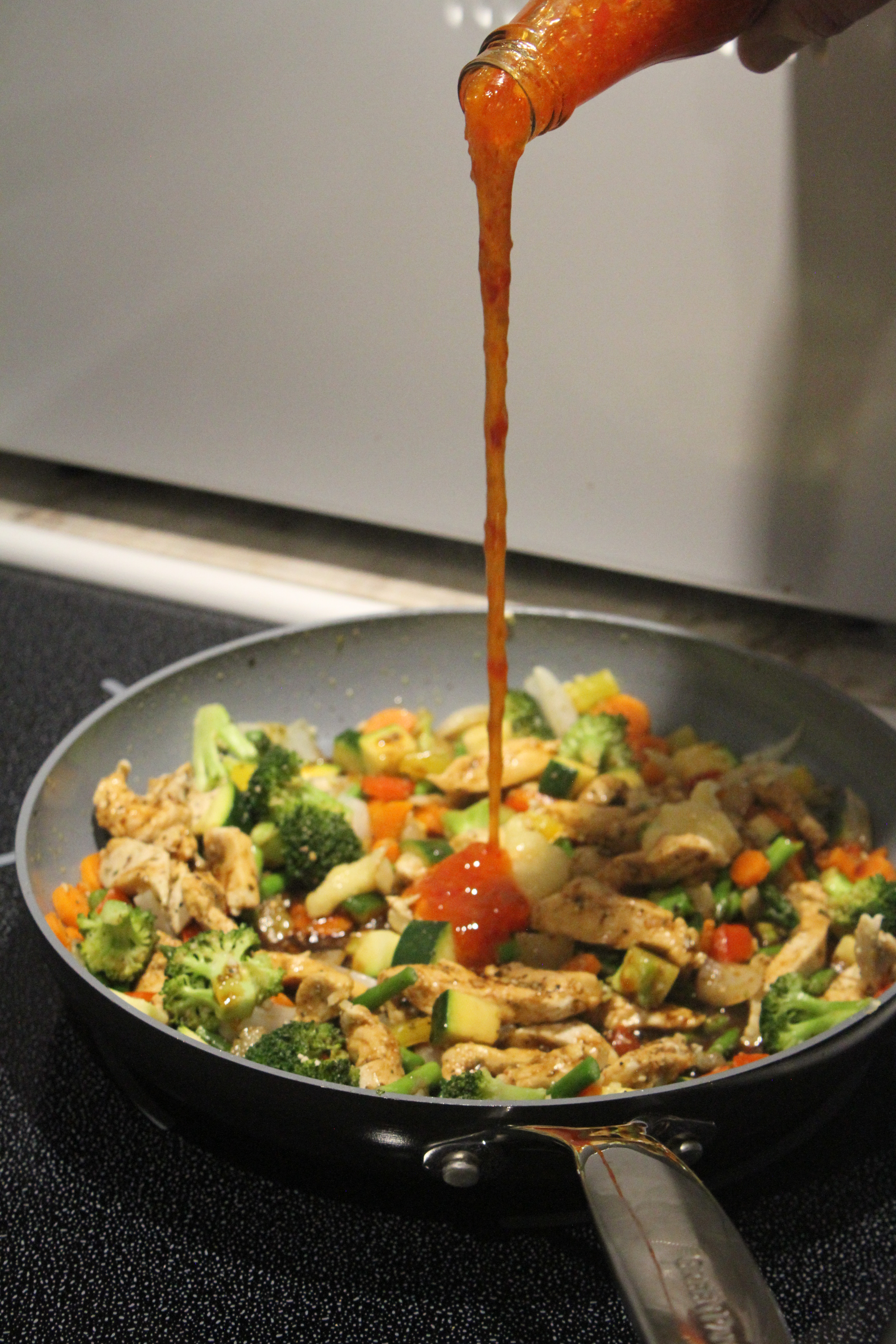 A beautiful sauce poor into a pan with stir fry in it. 